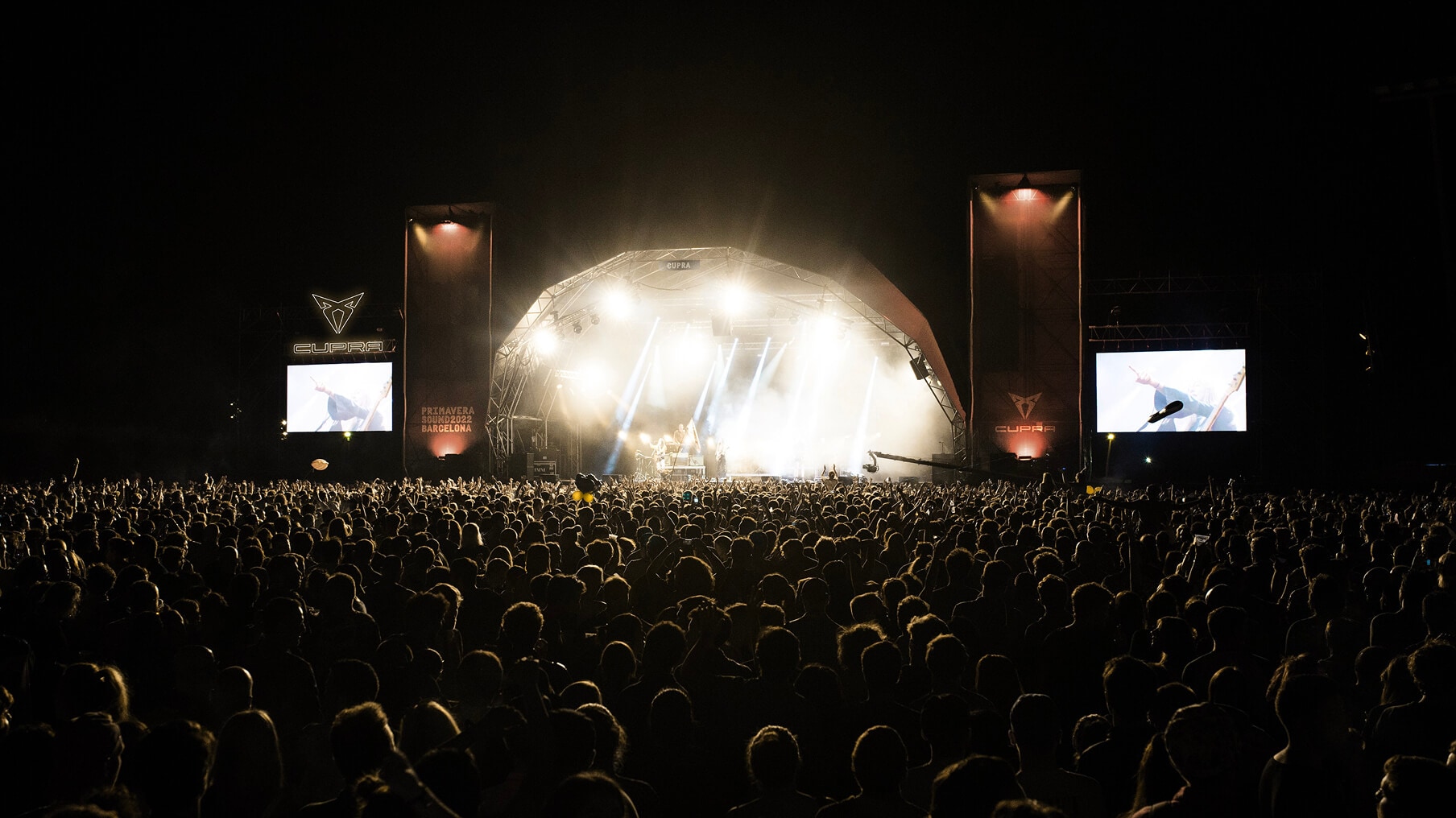 A concert stage is lit with orange lights and features the CUPRA logo on screens to the left, right, and center.