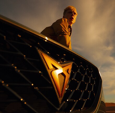 Close-up of the CUPRA badge under dramatic light, with the driver in the background—capturing the spirit of performance, identity, and freedom on the open road.